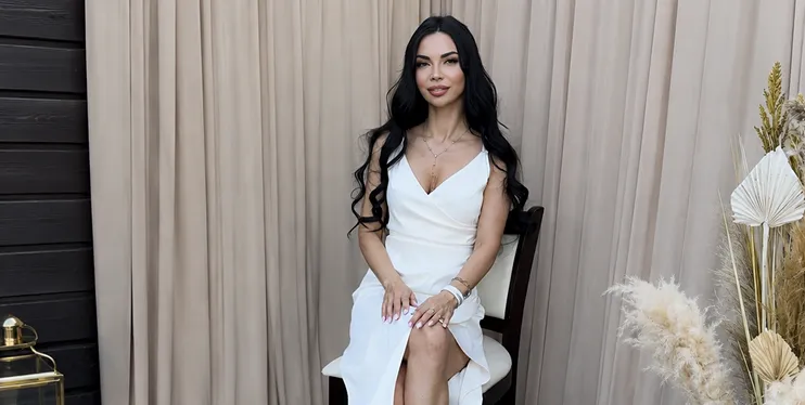 Iryna Ribeiro in a white dress on a chair against a beige backdrop