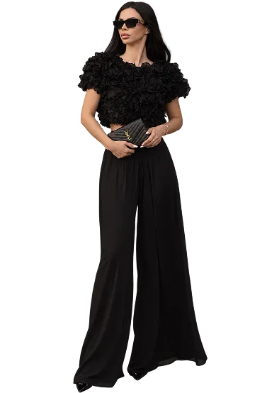 Iryna Ribeiro in a black ruffled top and wide-leg trousers