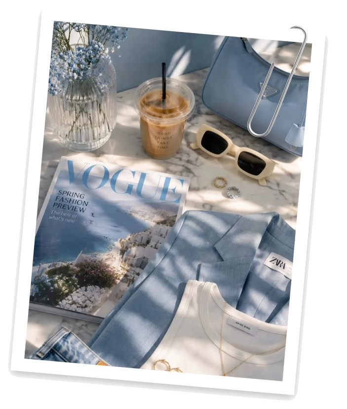 A blue blazer, a magazine, a bag and sunglasses laid out on a table