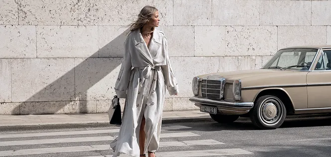 A woman in a long trench coat crossing a street