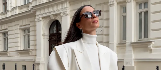 A woman in a white oversized suit with a burgundy clutch on a city street