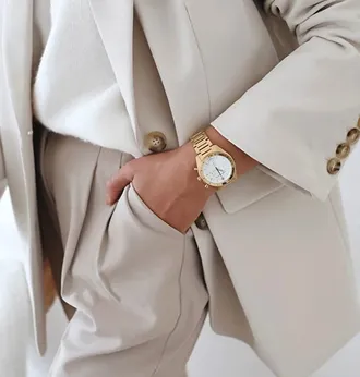 A beige tailored blazer and trousers worn with a gold watch