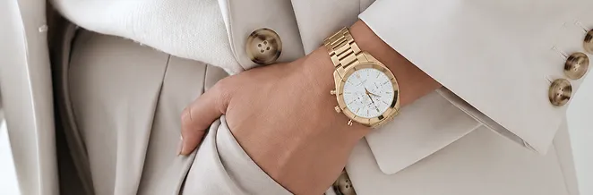 A beige tailored blazer and trousers worn with a gold watch