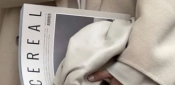 A fashion magazine and a cream leather bag on a beige coat