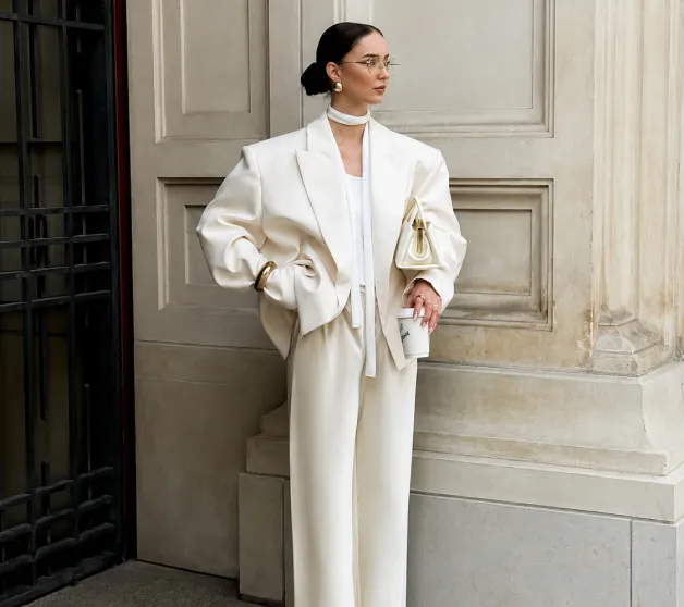 A woman in a cream suit with wide-leg trousers by a stone wall