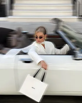 A woman in a white suit with a shopping bag stepping out of a car