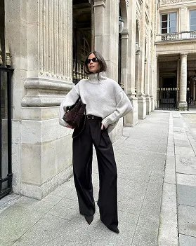 A grey knit jumper styled with black wide-leg trousers on a city street