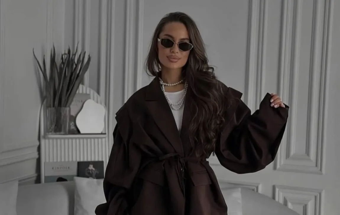 A woman in a brown belted coat in a light interior